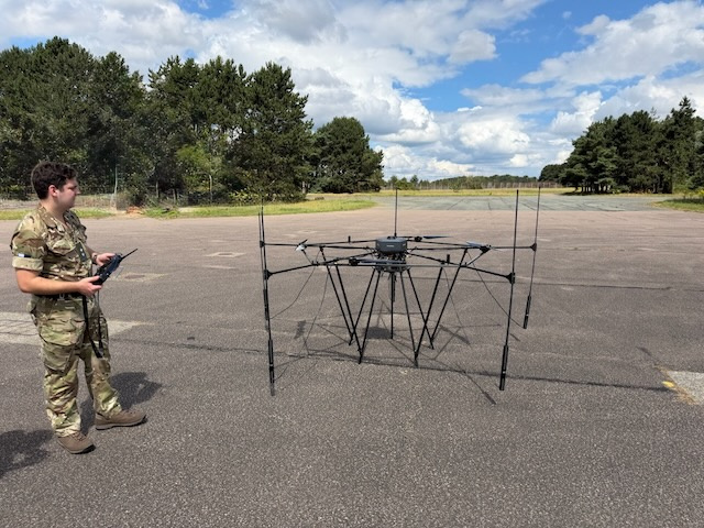 Person in military uniform holding a controller and looking at a drone outdoors