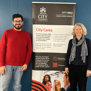 Two colleagues stand next to a City Cares, City St George’s, University of London’s dedicated support programme pull-up banner.