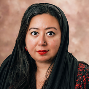 Mehwaesh Islam​​​​ wears a red and black top and is in front of a pale pink background.