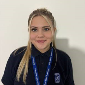 Olivia Marshall, Nuclear Engineering Technician Apprentice wears a black sweater and blue lanyard. She is standing against a white background.