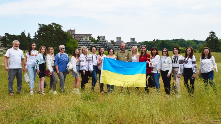 A group of 17 colleagues involved in the University of East Anglia and Vasyl Stefanyk Precarpathian National University Twinning partnership stand in a field holding a Ukraine flag.