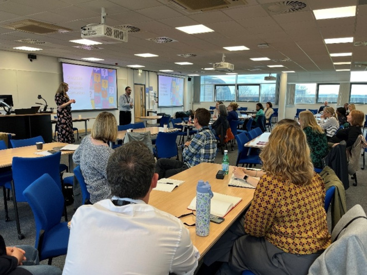 Colleagues are seated around tables, watching a presentation at the Building COIL capability in the UK and Ireland symposium, April 2025, University of Leeds