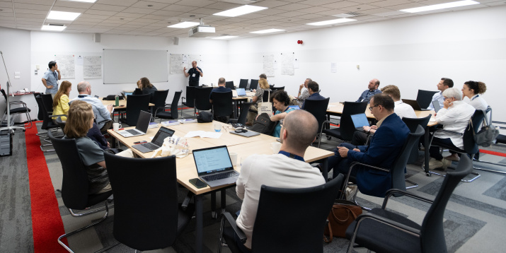 Researchers attend a workshop on regulatable artificial intelligence. They're seated around tables, listening to a speaker at the front of the room.