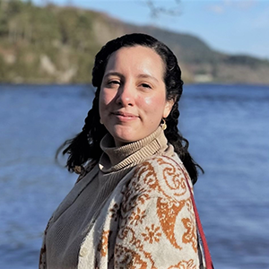 Ana María smiling and standing in front of mountains and water