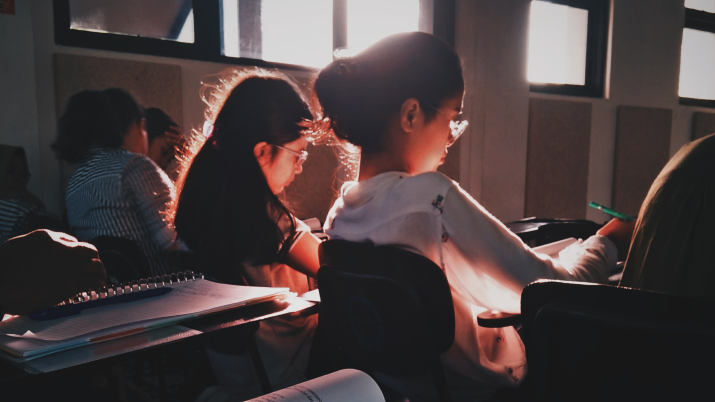 Students learning in a classroom, a bright white sunshine behind them 