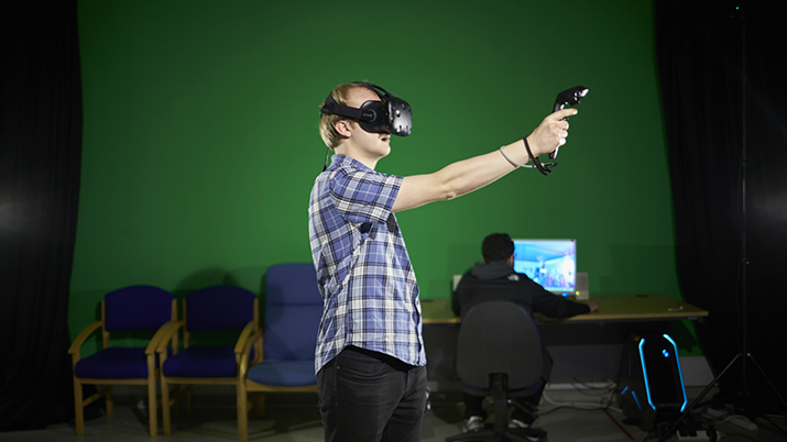 A student is wearing a headset and holding out a controller against a green background.