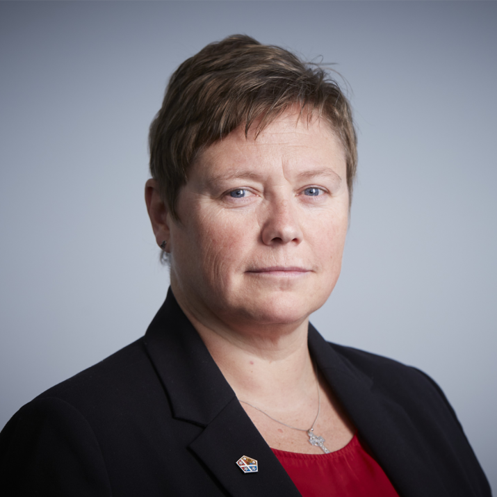 Gillian Docherty standing against a grey background. Gillian wears a black blazer and red top.