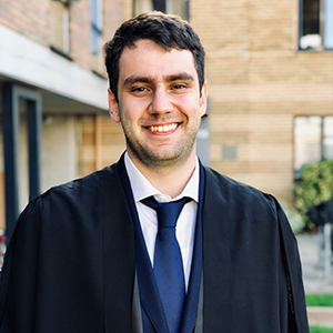 Horia smiling. He is wearing a suit and graduation gown.
