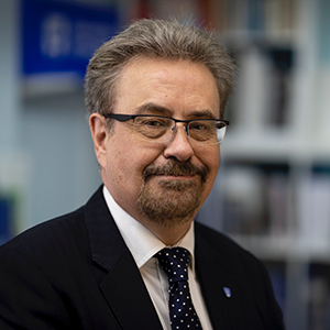 Iain Gillespie smiling against an office background. He is wearing a suit and tie.