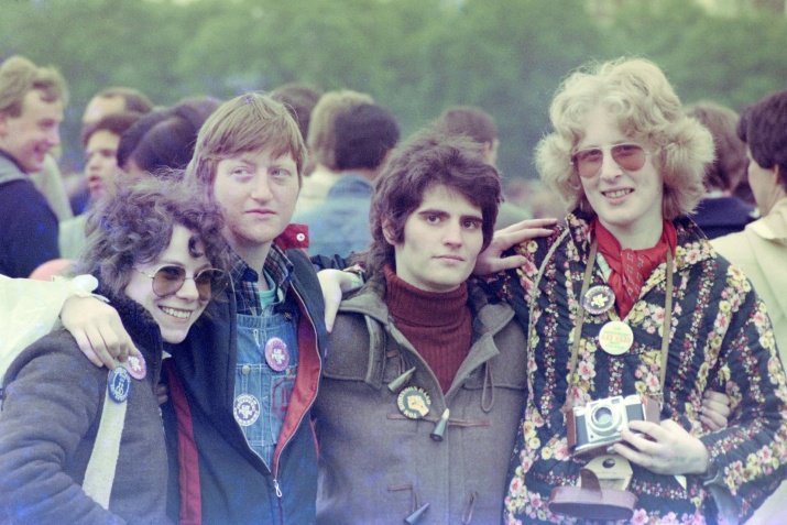 Four young people standing with their arms around each other at Gay Pride 1979. They are wearing badges with political slogans.