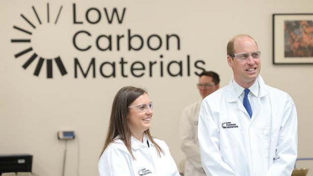 Prince William and Natasha Boulding in white lab jackets. They stand in a lab in front of a wall with the Low Carbon Materials logo.