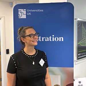 Magda Graszka smiling at a Universities UK event in front of a banner with the word 'registration' on it