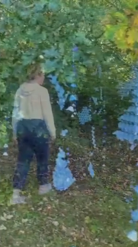 A figure walking through an installation art piece made from blue egg crates in a forest