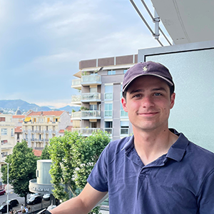 Tom Lewis smiling and standing on a balcony with buildings and mountains behind