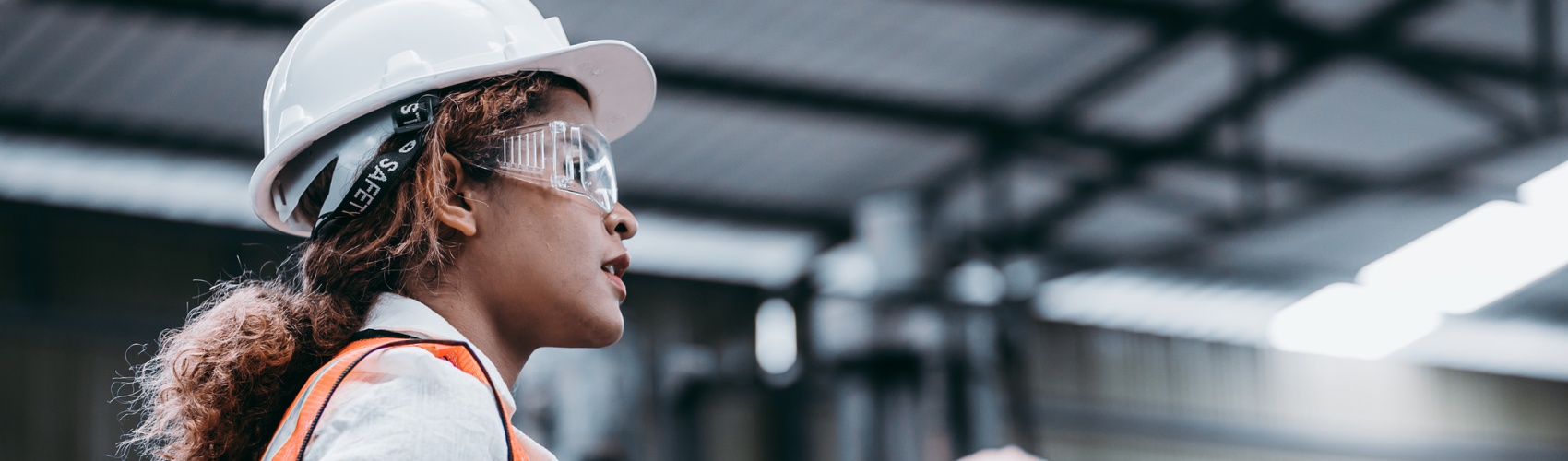 Female industrial engineer wearing a white helmet while standing in a heavy industrial factory behind she talking with workers, Various metal parts of the project
