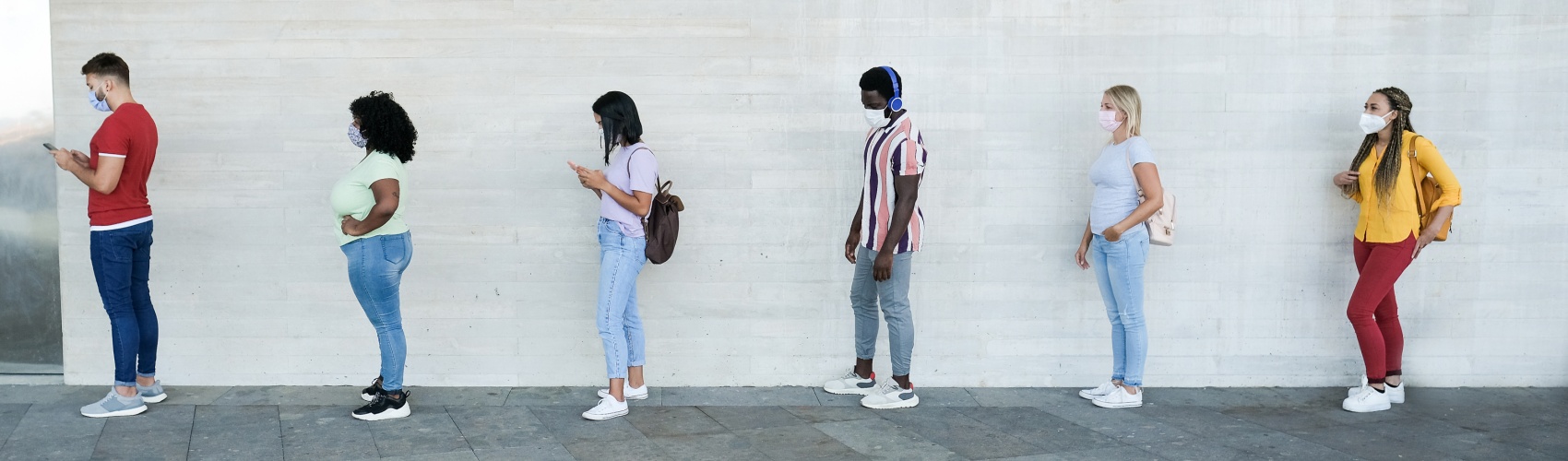 Multiracial people standing in a queue and waiting - Young people with social distancing and wearing protective face masks - Concept of the new normality and social distancing