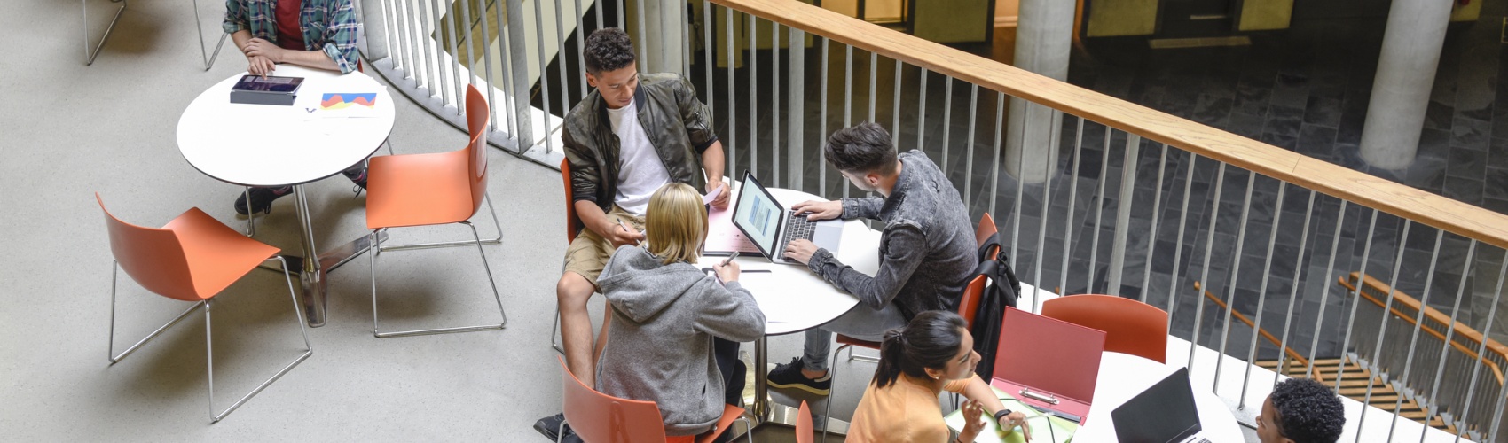 Students sitting at tables using laptops and meeting friends 