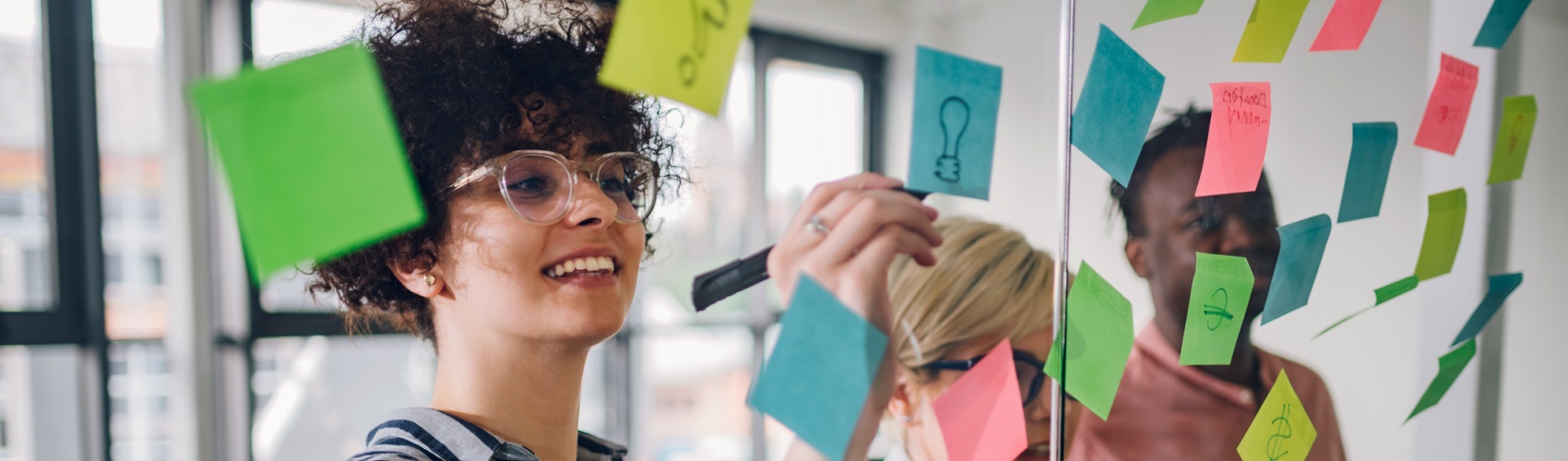 Team of three writing ideas on colourful sticky notes on a glass wall