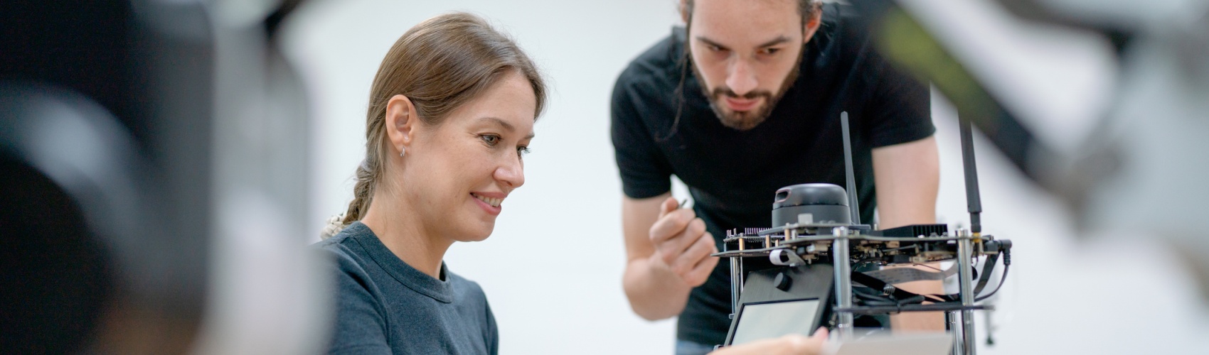 Two students at a desk with engineering equipment in front of them. The female student is adjusting the equipment and the male student leans over to observe.