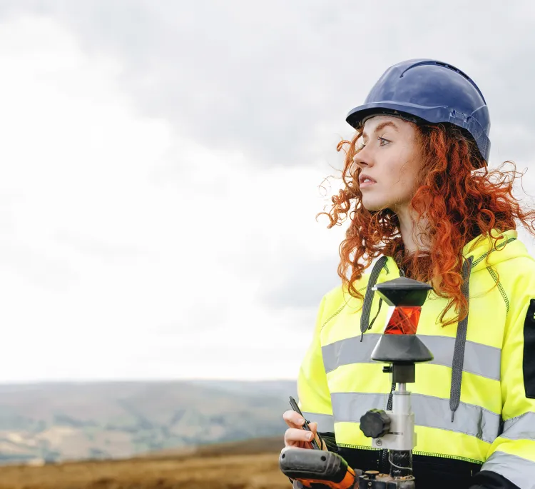 Woman wearing a hard hat and safety jacket in a hilly landscape