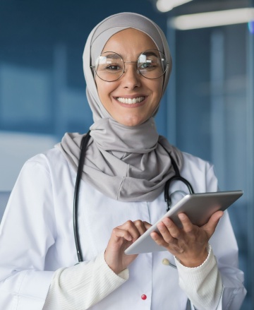 Female doctor wearing a hijab and glasses holding a touchscreen device.