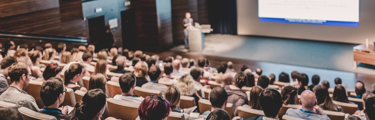 A lecturer delivering a lecture to a lecture room full of students through a digital presentation. 