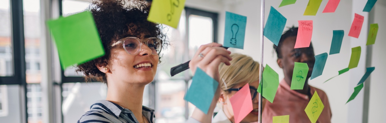 Team of three writing ideas on colourful sticky notes on a glass wall