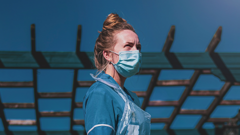 A nurse in a face mask stands against a clear sky